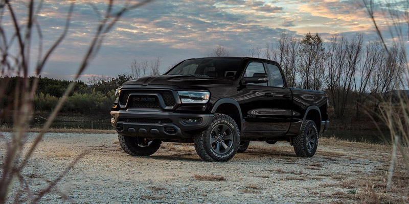 A black RAM pickup truck parked on a gravel road at sunset, showcasing its rugged design and off-road tires